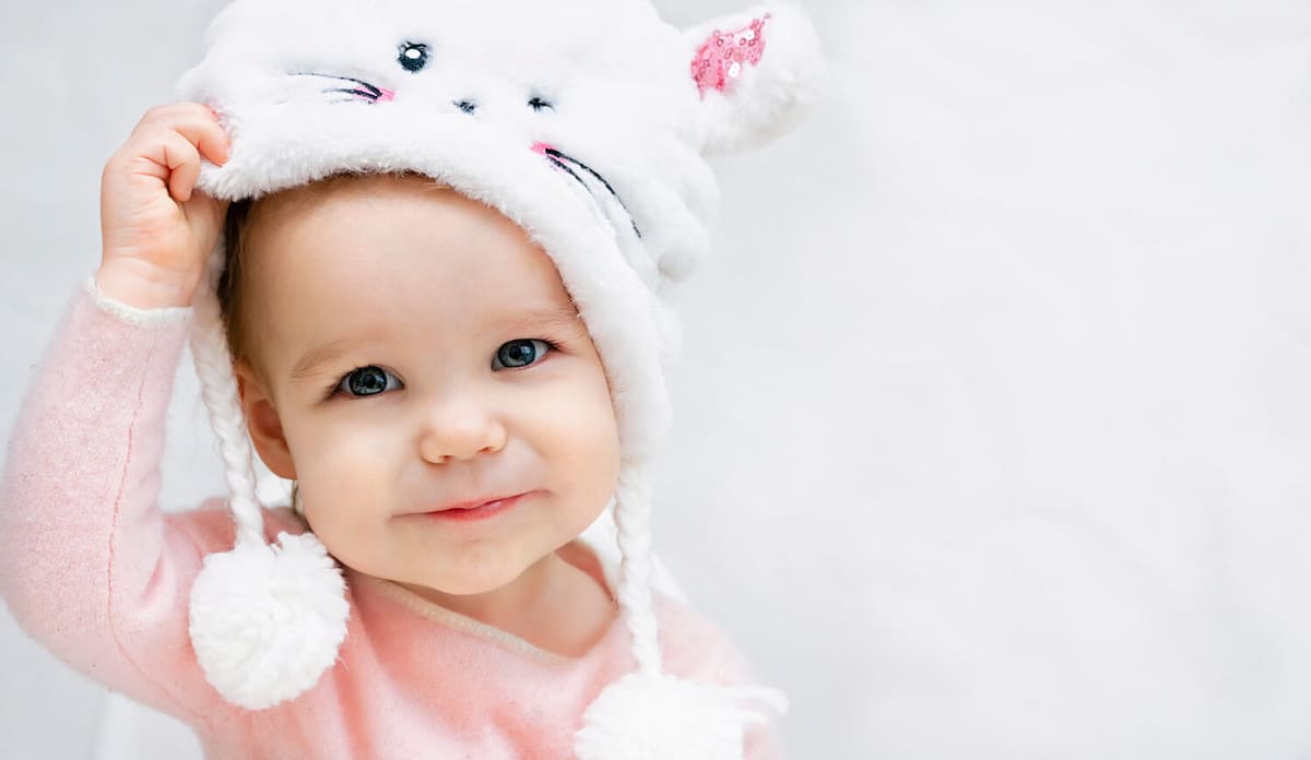 Portrait of a little girl child takes off or puts on a fluffy fur hat. Change of weather seasons, children's clothing and accessories, discount sale