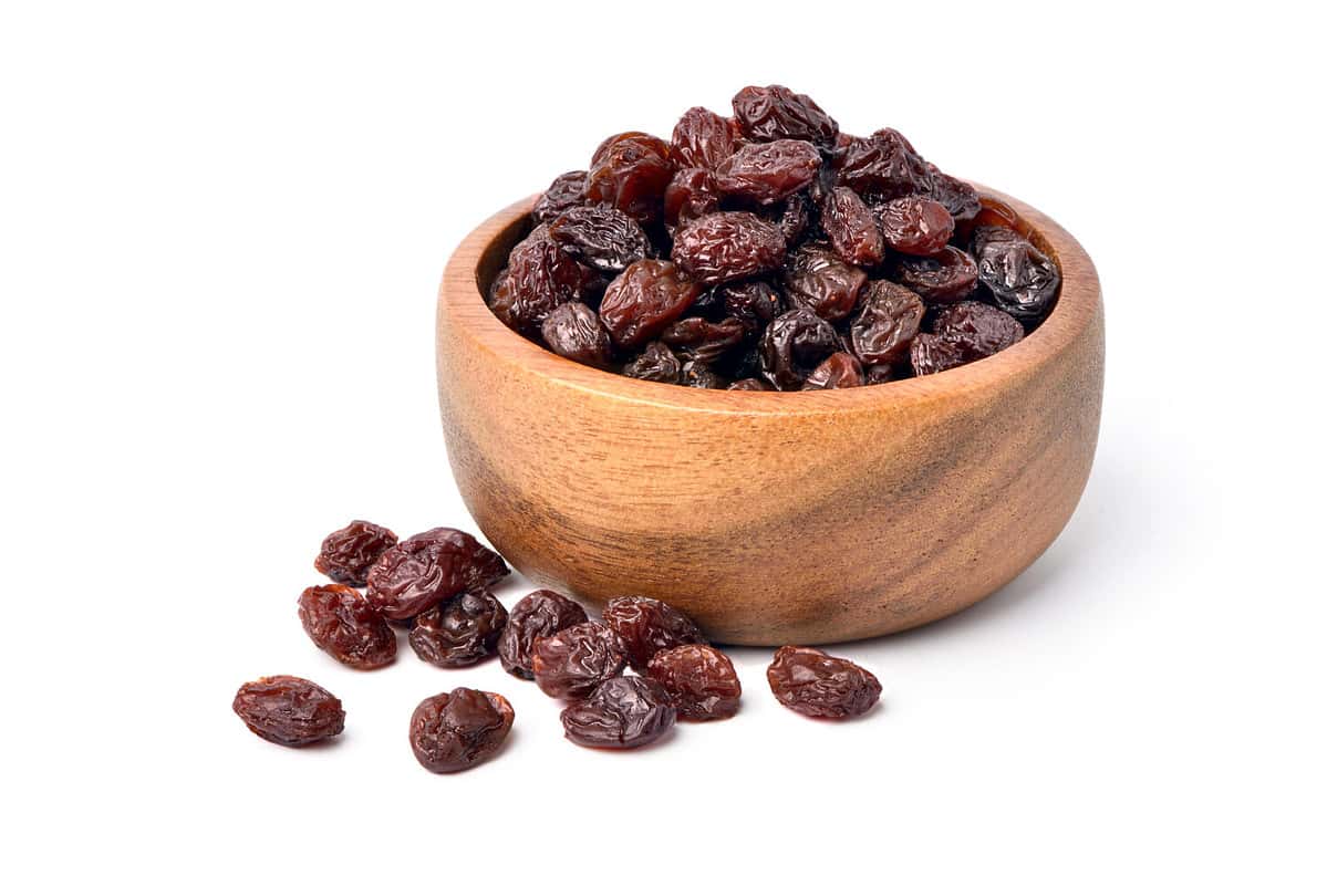 Raisins in wooden bowl isolated on white background.