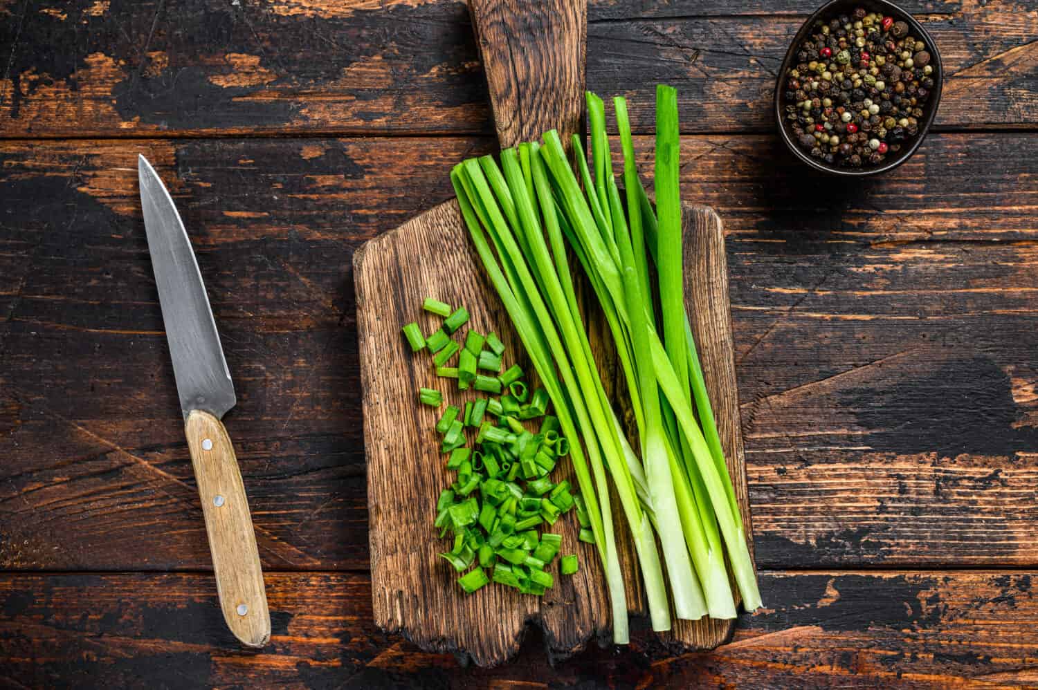 Cut Green onions chives on a cutting board. Dark wooden background. Top view.