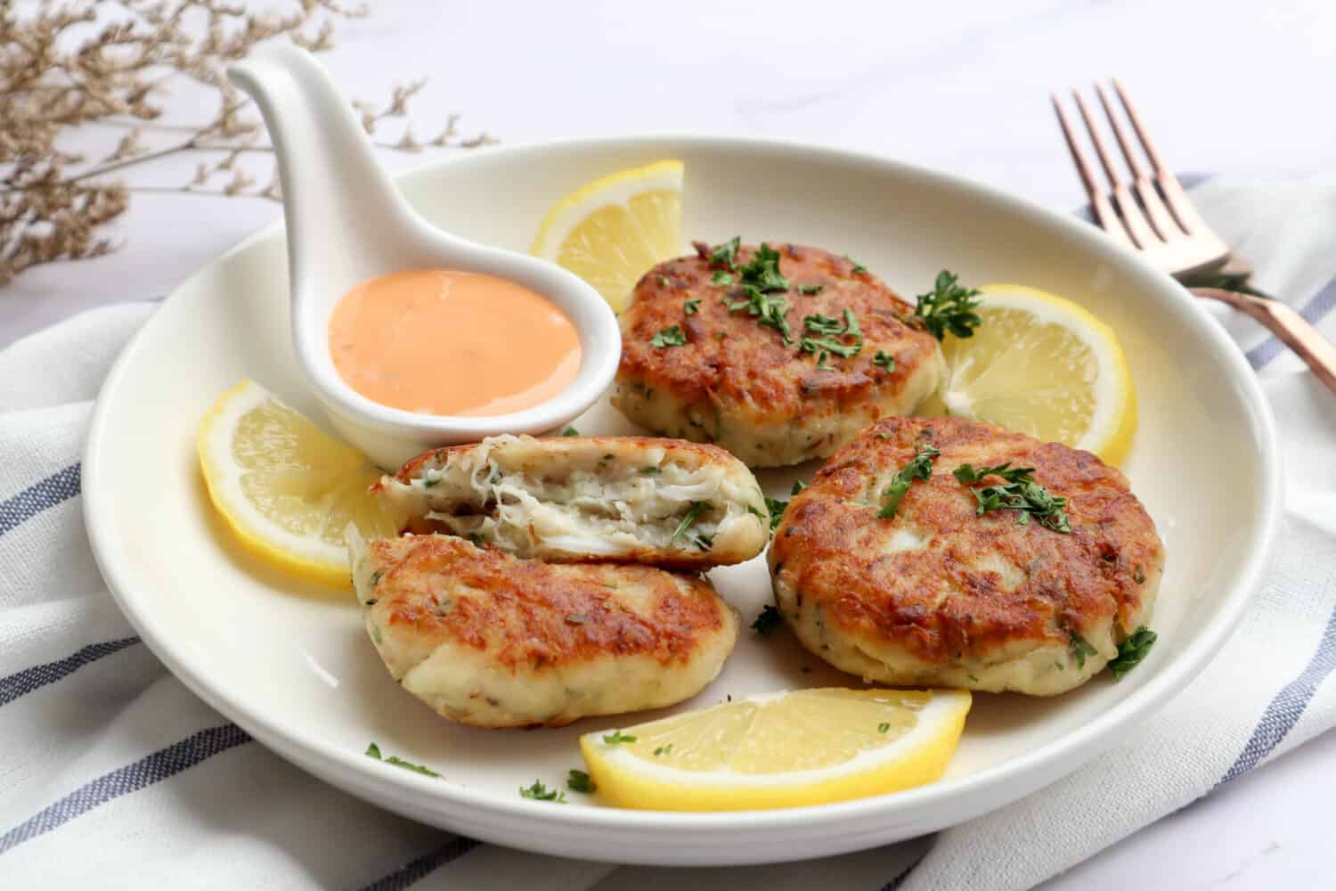 Crab cake with remoulade sauce and lemon in a white plate at close up view - healthy seafood appetizer
