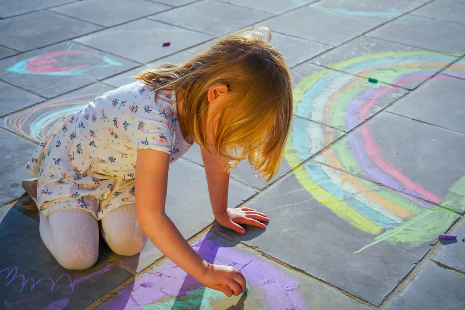 4 year old girl drawing a rainbow with chalks on floor