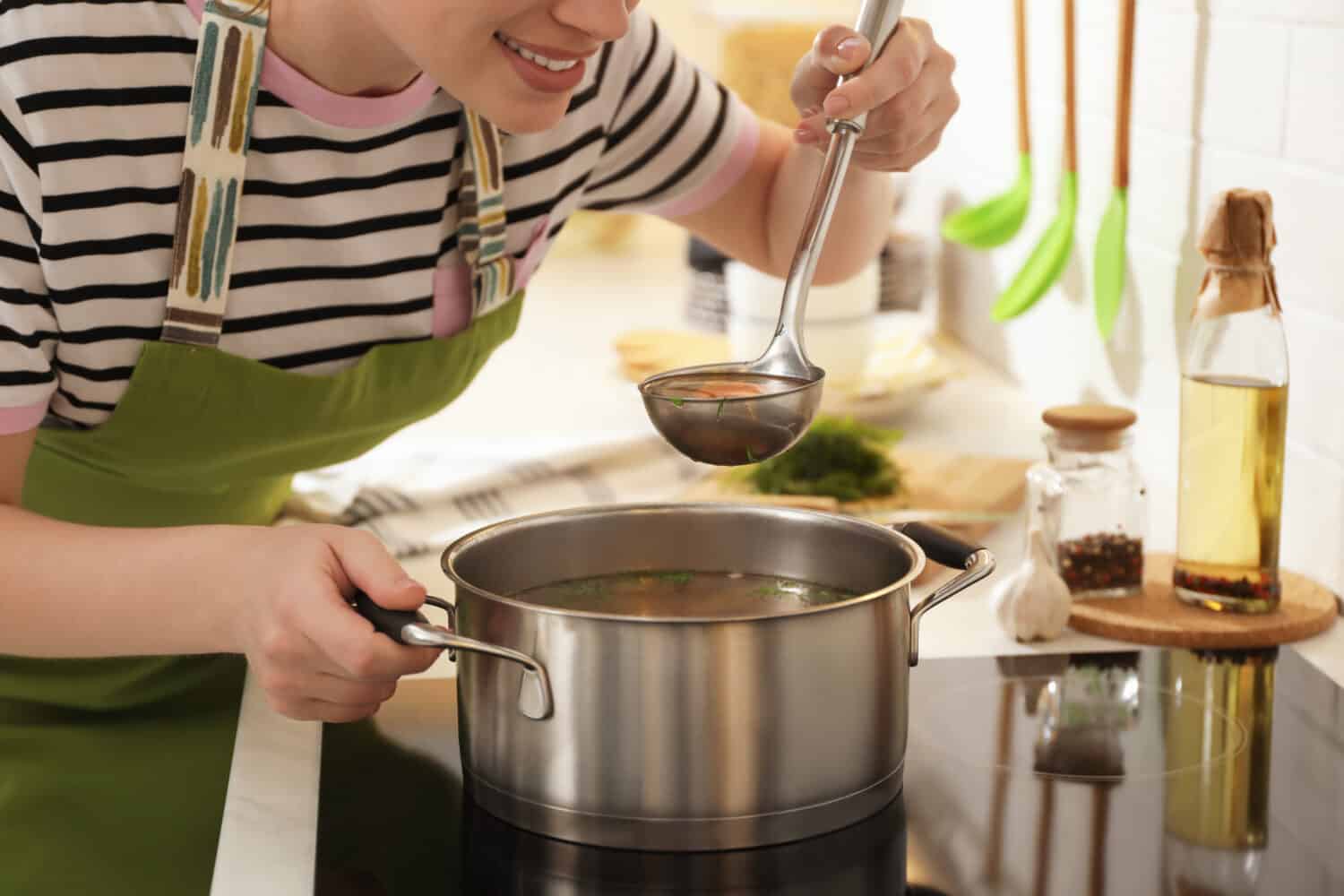 Woman making bouillon on stove in kitchen, closeup. Homemade recipe