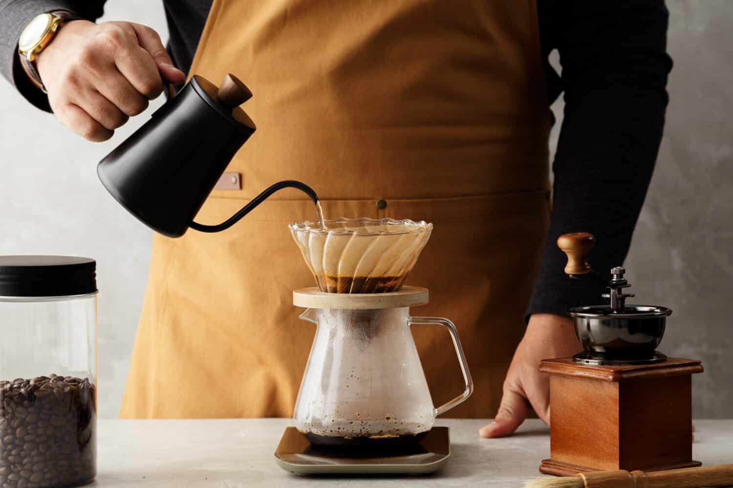 Men barista making a drip coffee, pouring hot water from kettle over a ground coffee powder