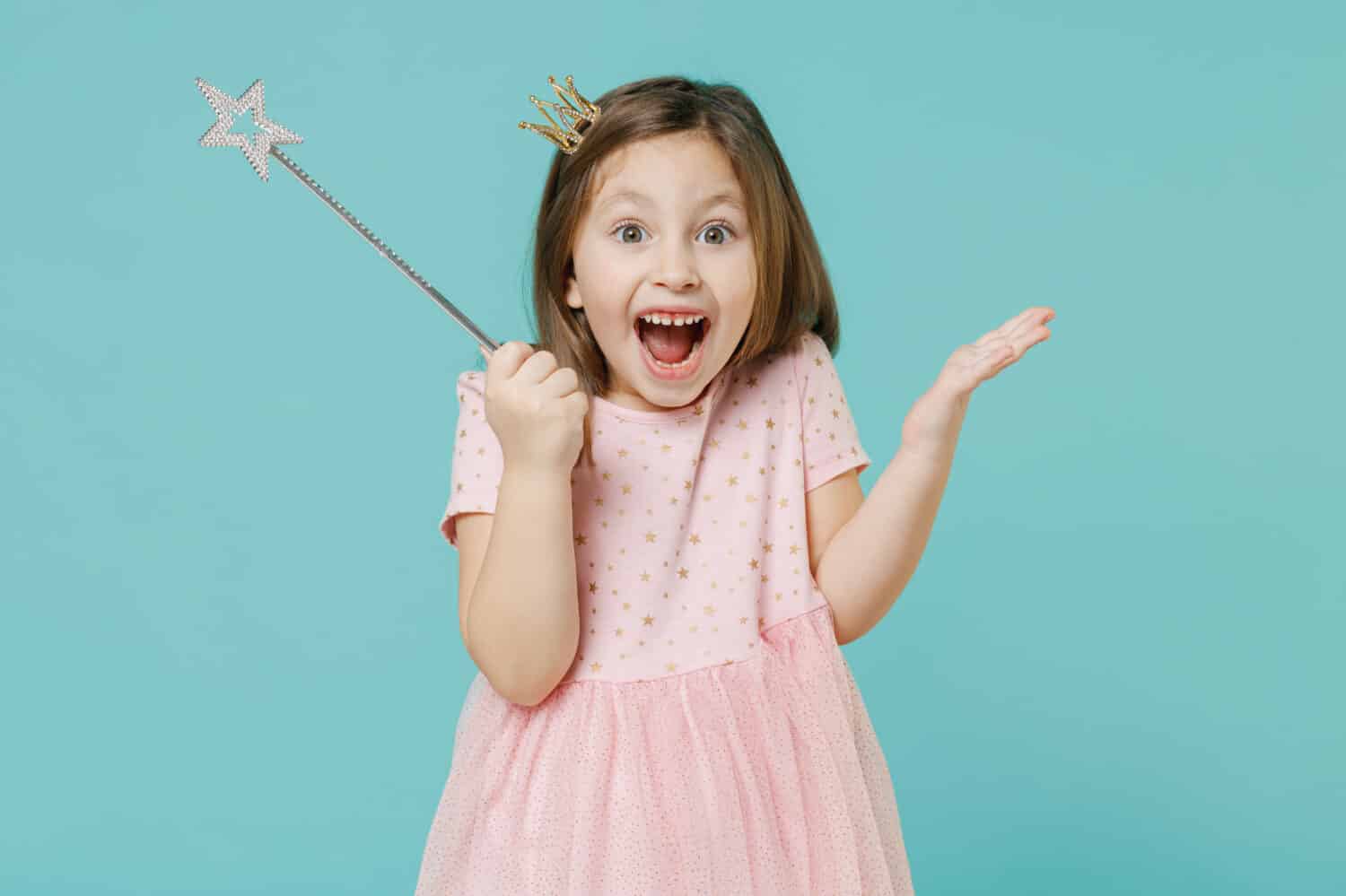 Little fun kid girl princess 5-6 years old wears pink dress crown diadem hold magic wand fairy stick isolated on pastel blue color background child studio. Mother's Day love family lifestyle concept