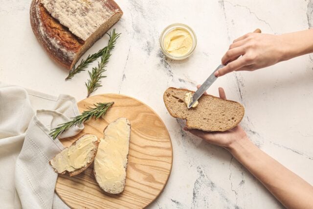 salted vs unsalted butter: Woman spreading butter onto slice of fresh bread on light background
