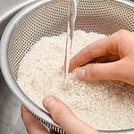 Woman rinsing rice in sifter under running water, closeup