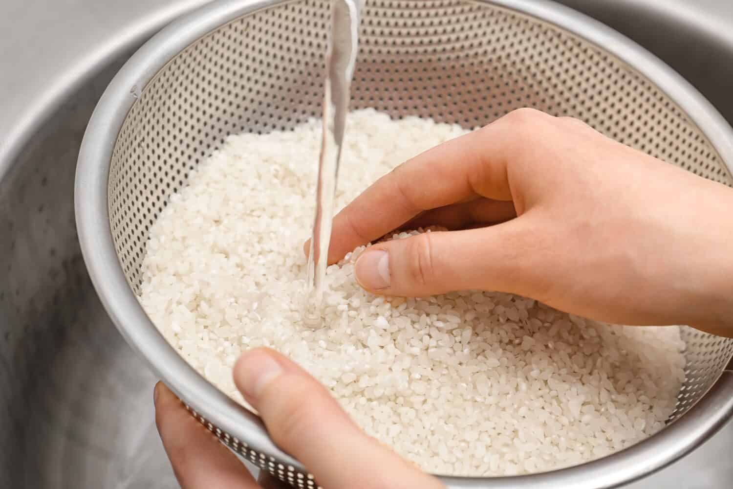 Woman rinsing rice in sifter under running water, closeup