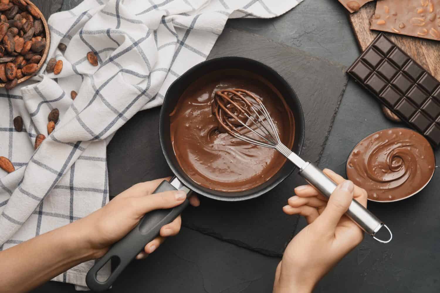 Woman cooking tasty melted chocolate on table in kitchen