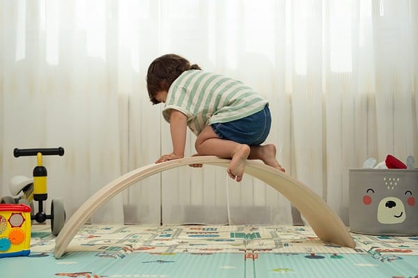 Rear view of a toddler climbing on a balance board in a montessori playroom.