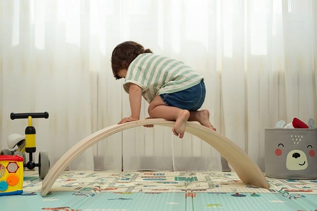 Rear view of a toddler climbing on a balance board in a montessori playroom.