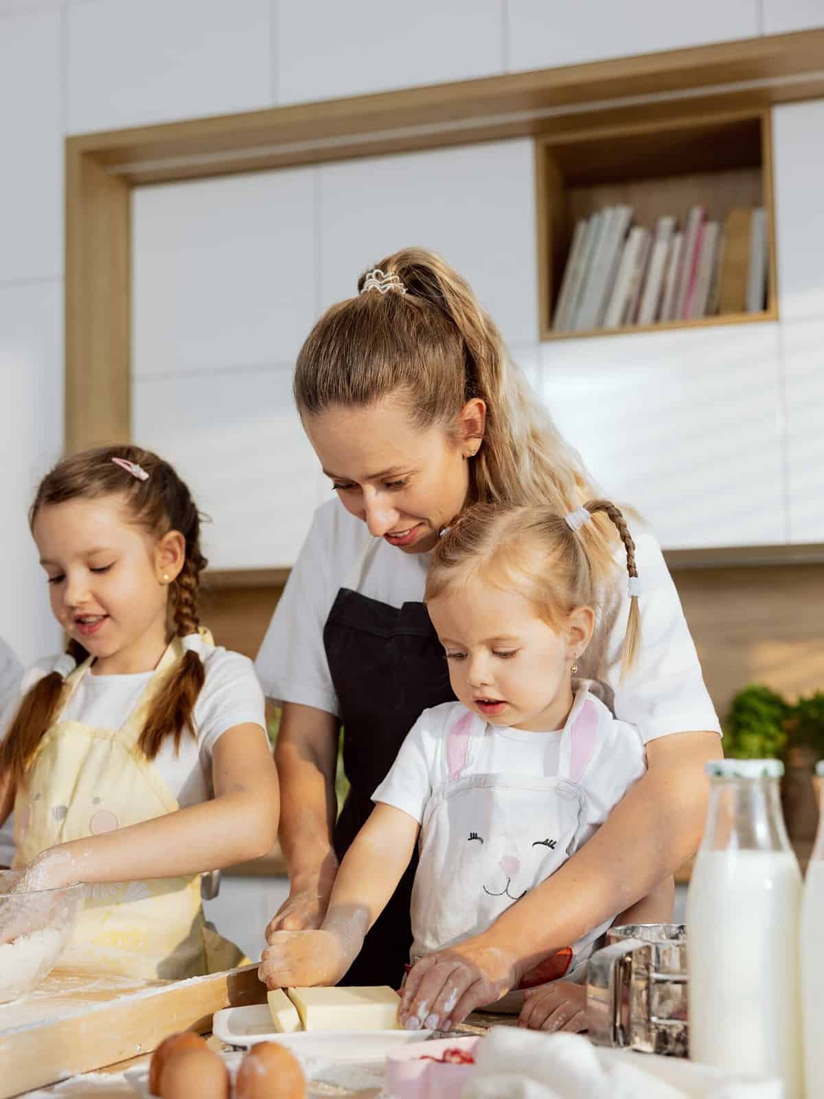 Salted vs Unsalted Butter: Excited preschooler daughter with young mother cutting butter with knife together in modern kitchen. Older kid kneading dough mixing eggs and flour. Family preparing dough for domestic pizza.