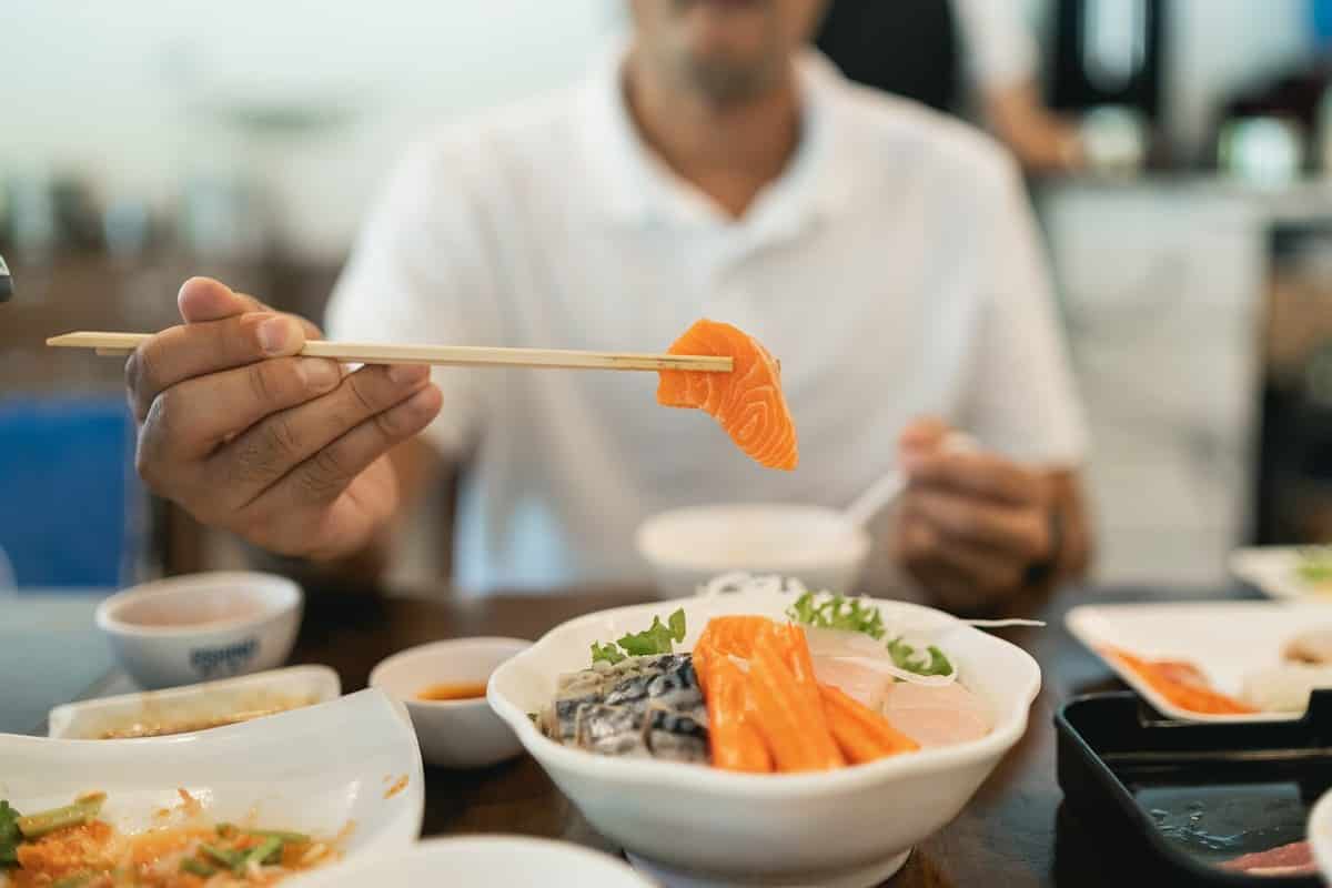 Asian man eating a sashimi salmon. Man using chopstick to pick raw fish sashimi from white bowl. Man using chopsticks sliced raw salmon, Japanese food in a japanese restaurant.