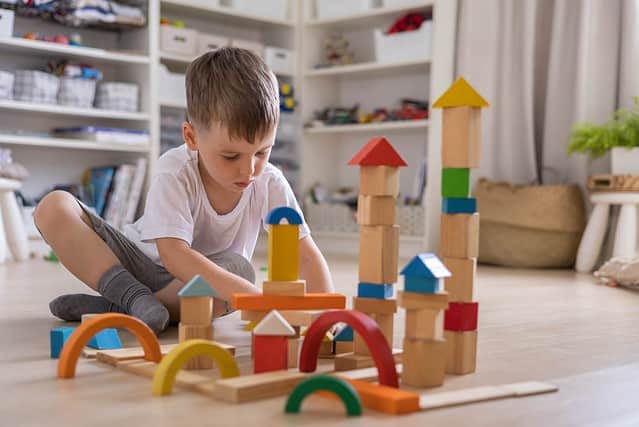 Confident male kid building fortress tower architecture wooden bricks ecology Montessori material. Baby boy playing construction eco friendly rainbow bricks at nursery childish room home toys storage