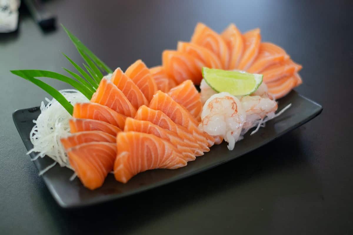 Salmon Sashimi in Japanese buffet restaurant menu. Fresh Sashimi fillet on black plate salmon slices. Salmon sashimi. Asian Food Menu. Seafood sashimi. focus on salmon sliced in the middle.