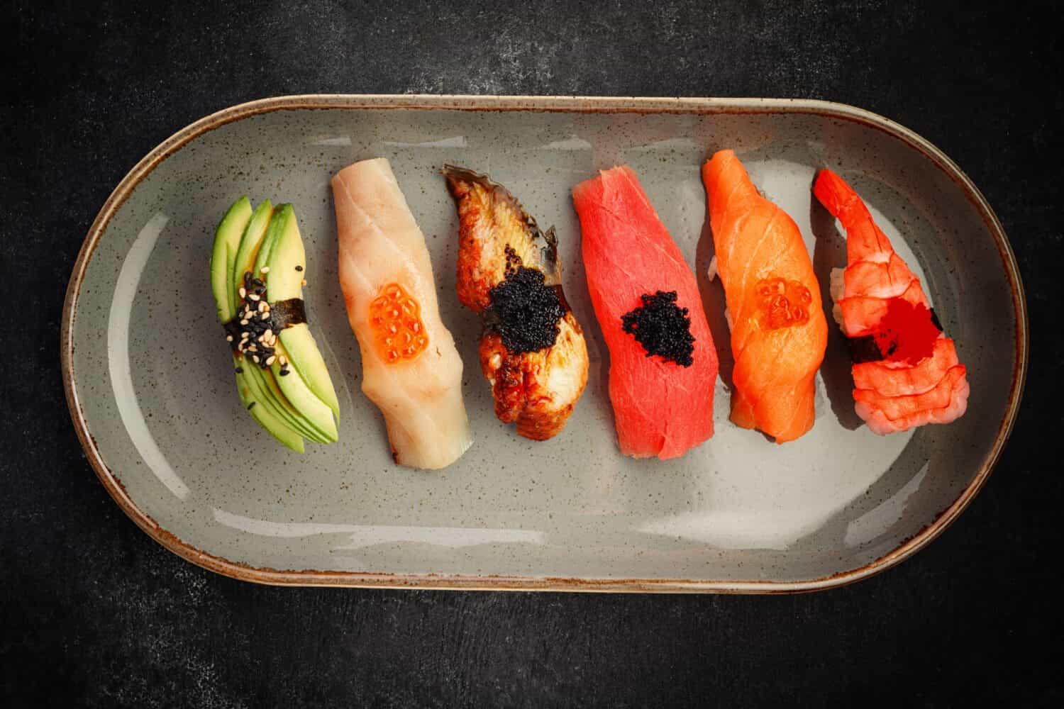 Assorted Nigiri sushi on a plate, on dark concrete. Top view