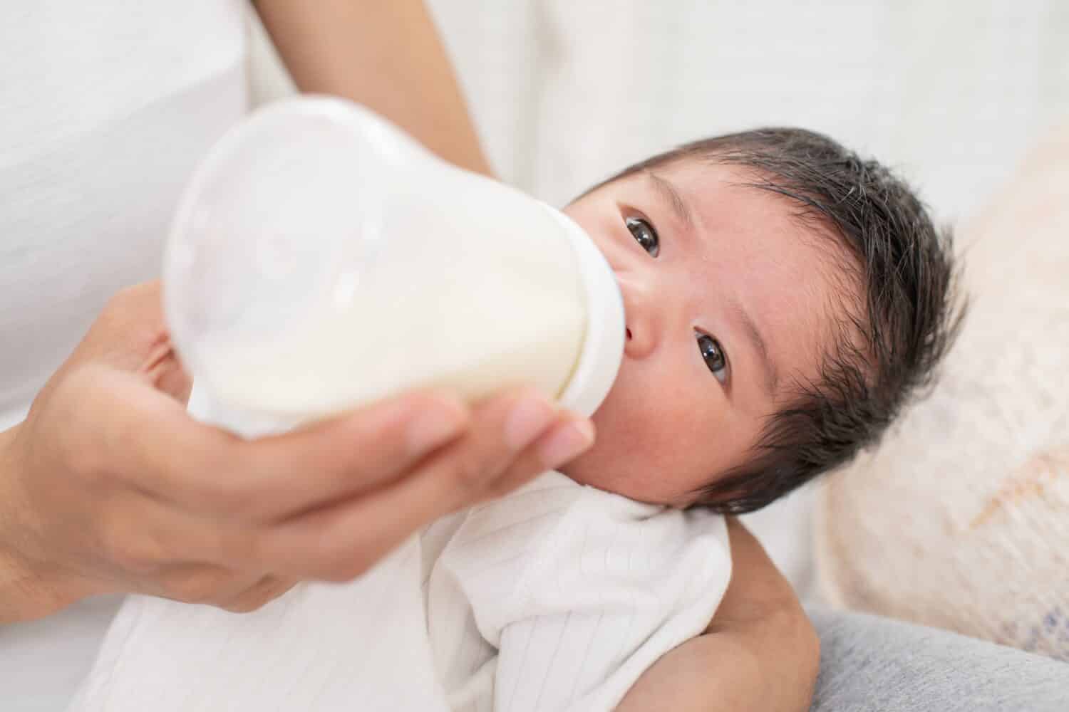 mother feeding baby boy with fresh milk in plastic bottle in bed closeup. mother breastfeeding and hugging baby. Lactation infant concept.