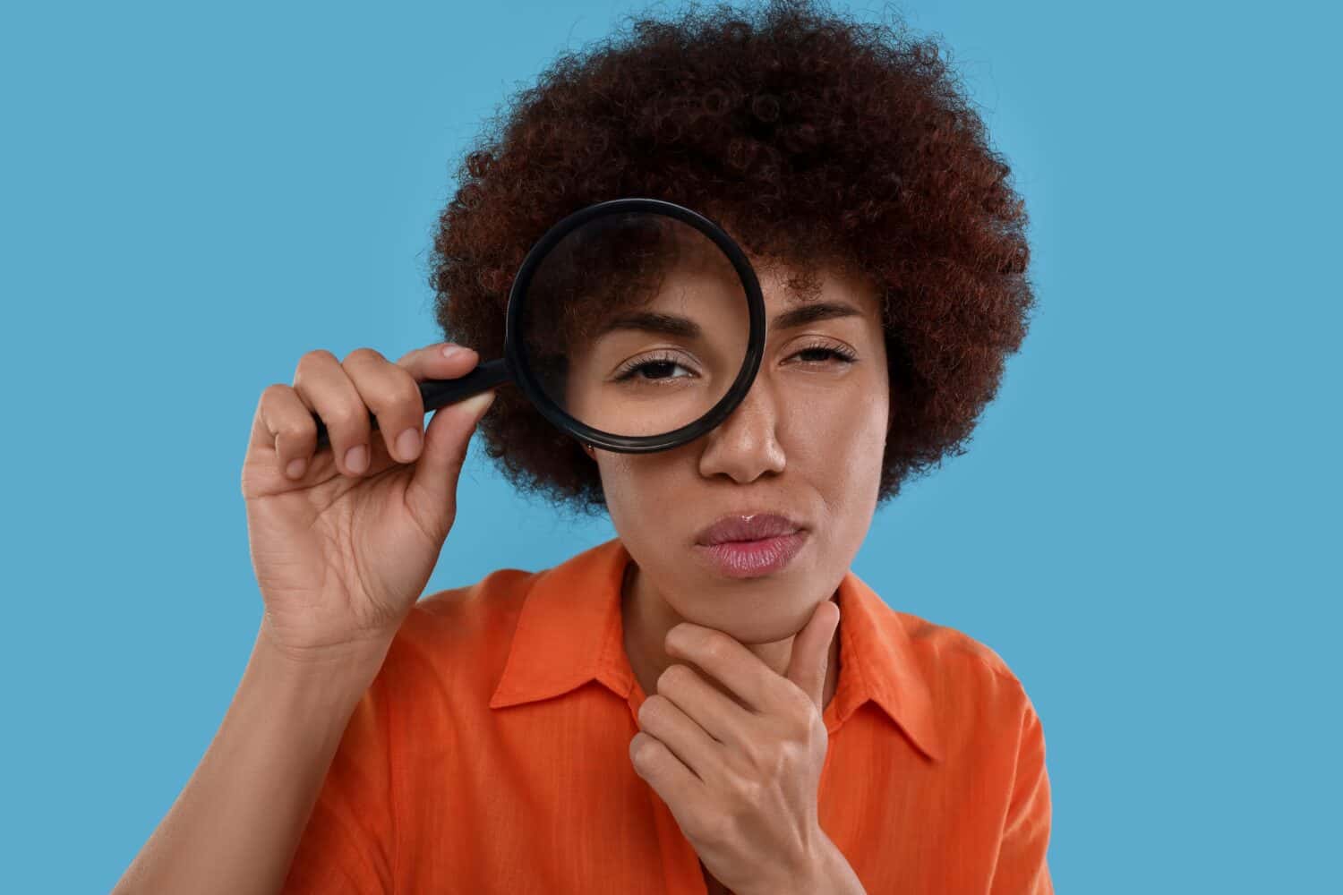 Young woman looking through magnifier glass on light blue background