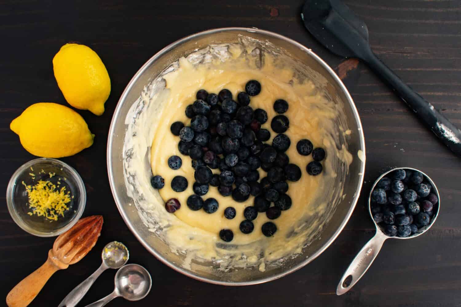 Mixing Bowl Filled with Muffin Batter and Fresh Blueberries: Bowl of blueberry muffin batter surrounded by fresh ingredients and kitchen utensils