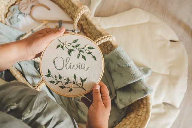 Pregnant woman holding a handmade embroidery with the name Olivia in her hands, concept in anticipation.
