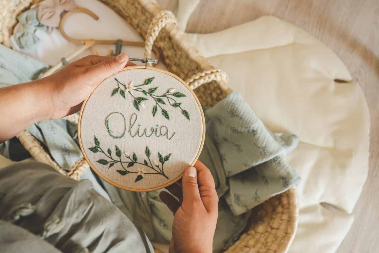 Pregnant woman holding a handmade embroidery with the name Olivia in her hands, concept in anticipation.