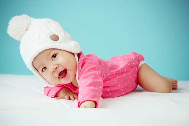 Little baby in knit winter clothing closing face with knitted beanie on the bed in the blue bedroom, New family and baby protection concept