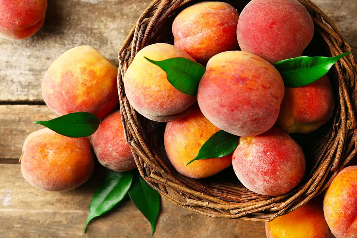 Ripe peaches in basket on wooden background