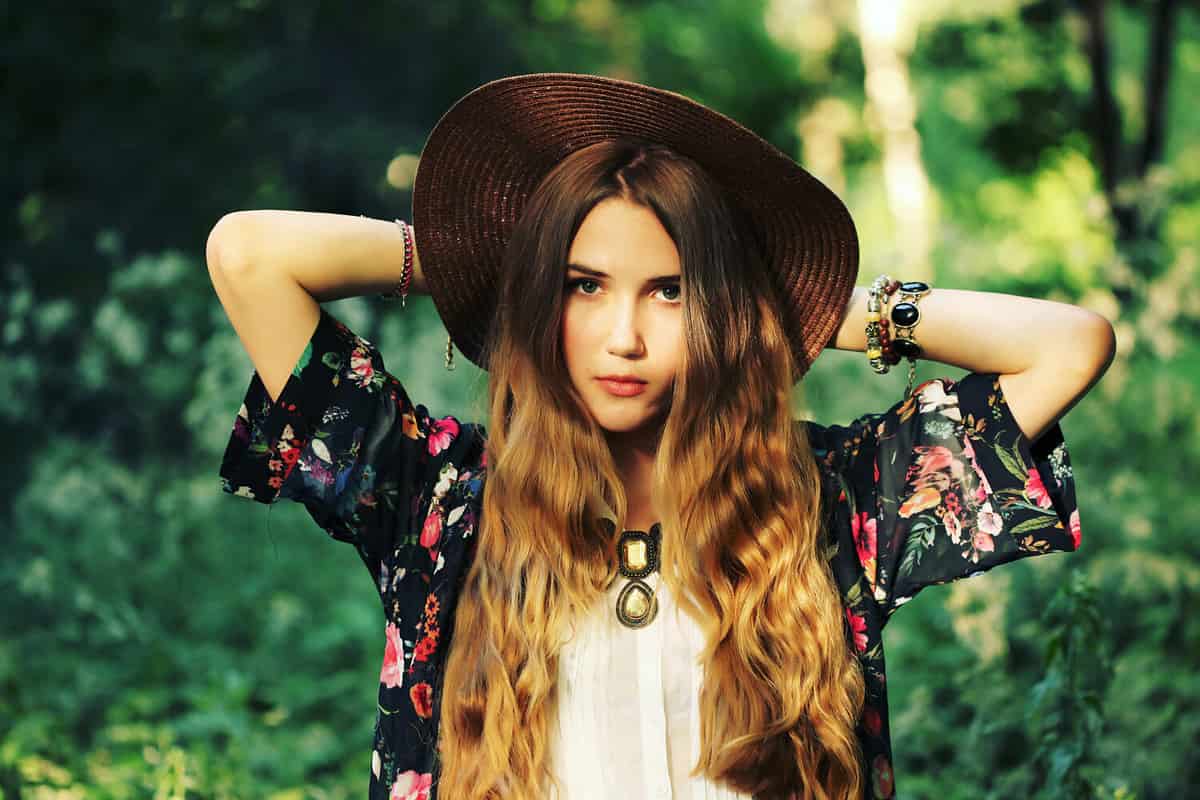 Fashion portrait of beautiful hippie young woman wearing boho chic clothes and summer hat outdoors. Soft warm vintage color tone. Artsy bohemian style.