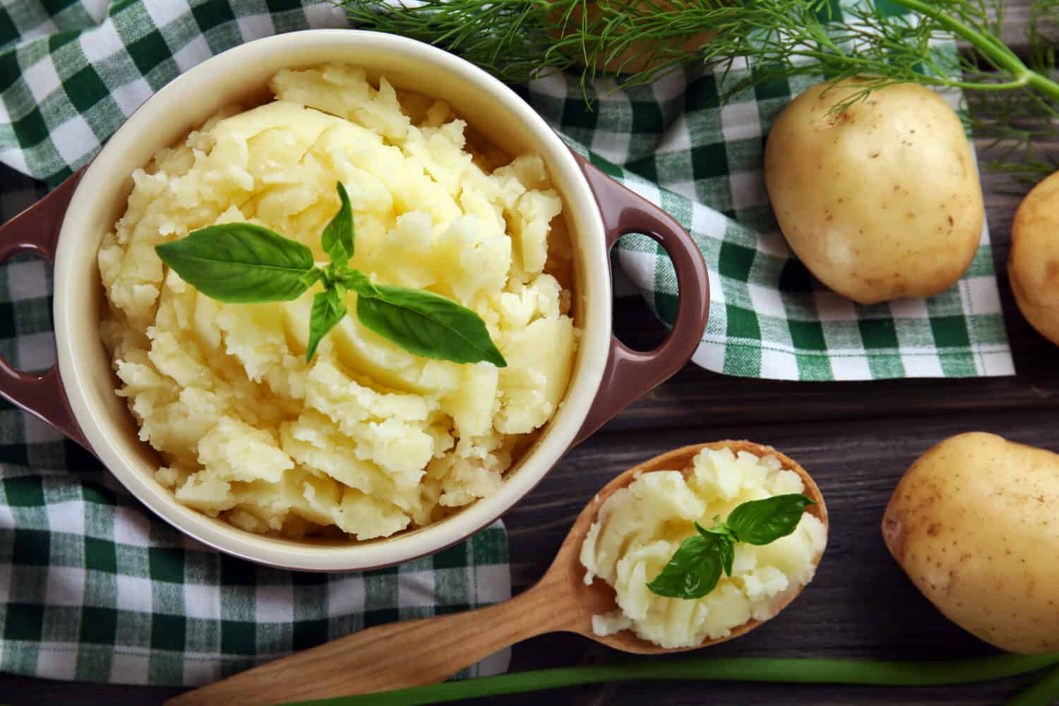 Mashed potatoes in bowl on wooden table with checkered napkin, top view