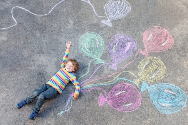 Cute little kid boy playing and flying with colorful balloons picture drawing with chalk. Creative leisure for children outdoors in summer, celebrating birthday