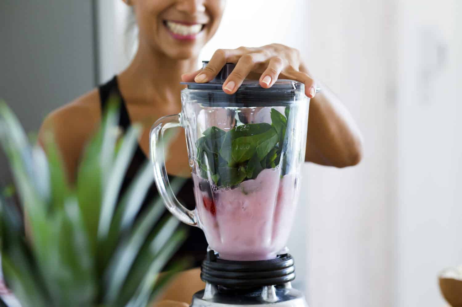 Woman blending spinach, berries, bananas and almond milk to make a healthy green smoothie