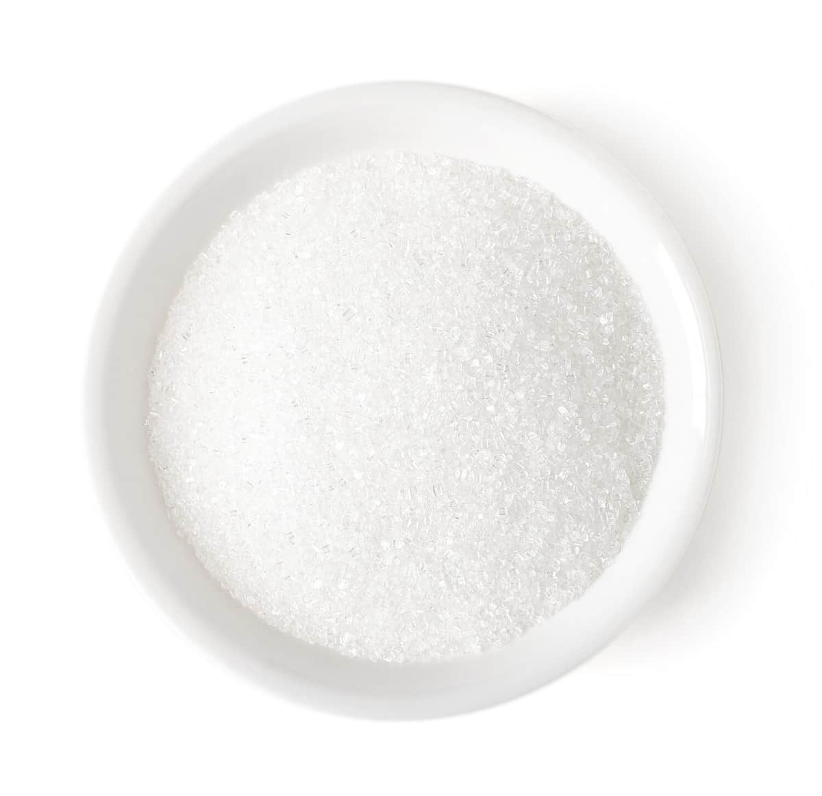 Bowl of white sugar isolated on white background, top view