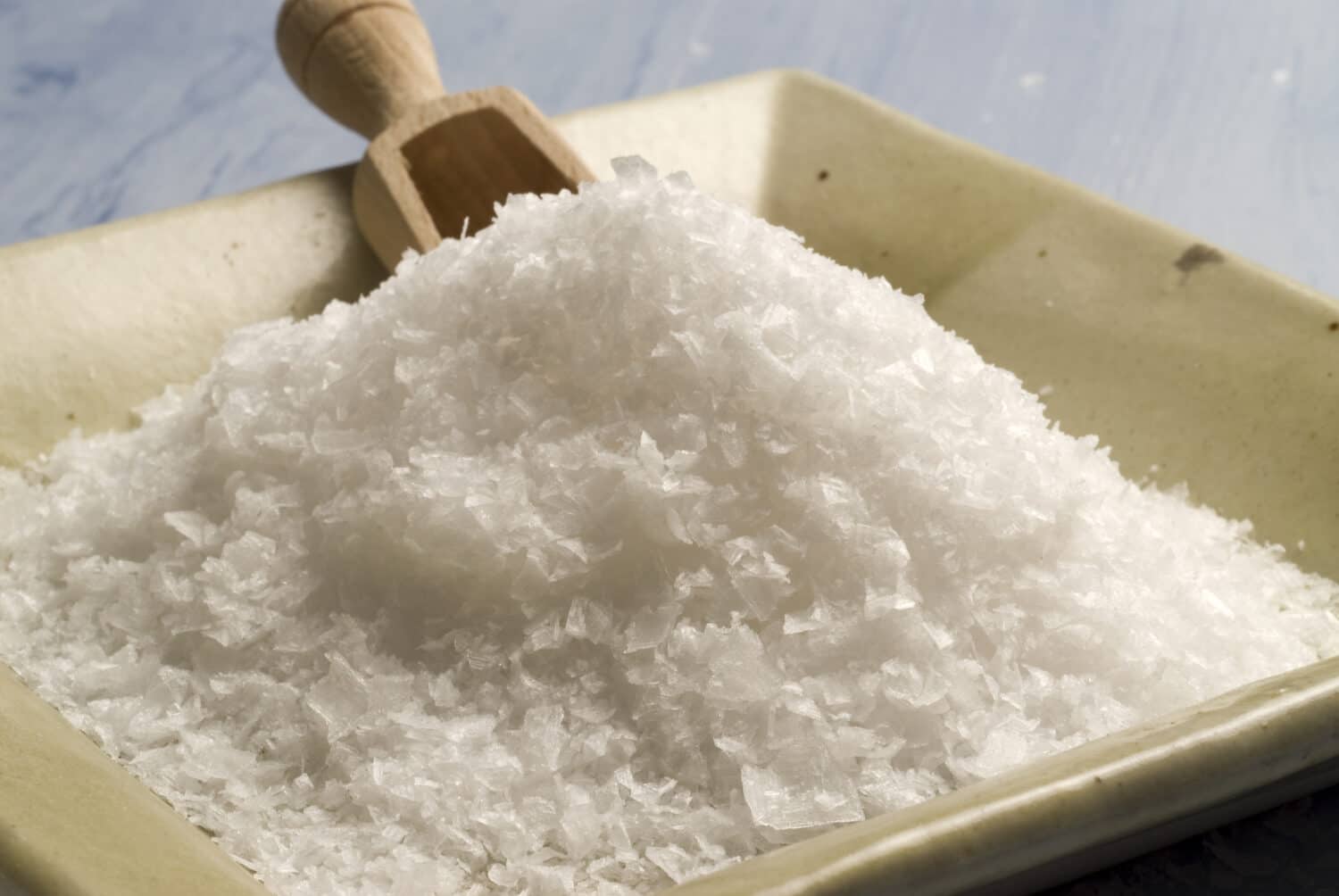 Maldon sea salt in a japanese ceramic plate. Blue background.Selective focus.