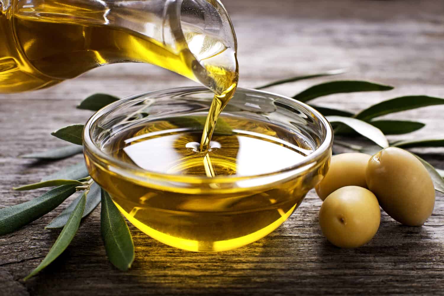 Bottle pouring virgin olive oil in a bowl close up