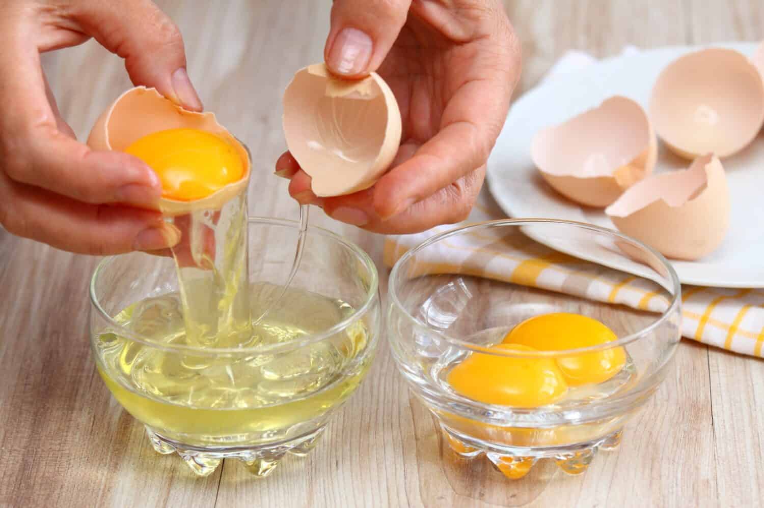 Woman hands breaking an egg to separate egg white and yolks and egg shells at the background