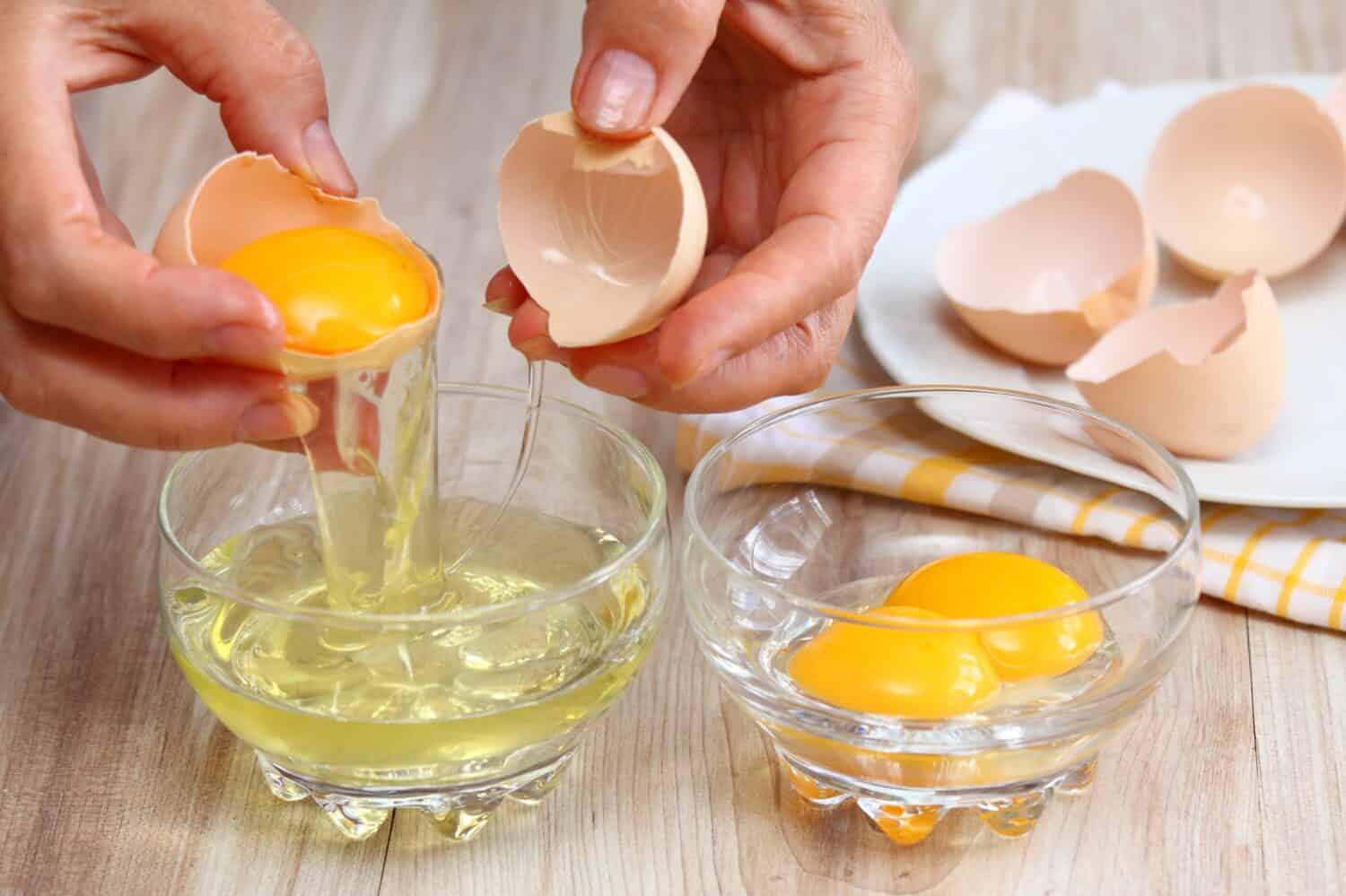 Woman hands breaking an egg to separate  egg white and  yolks and egg shells at the background  