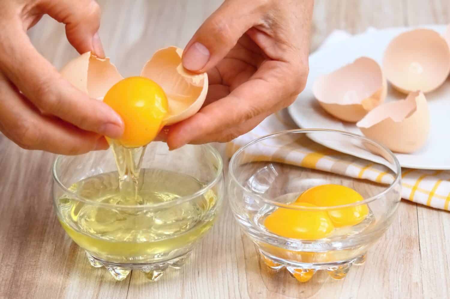 brown vs. white eggs Woman hands breaking an egg to separate egg white and yolks and egg shells at the background