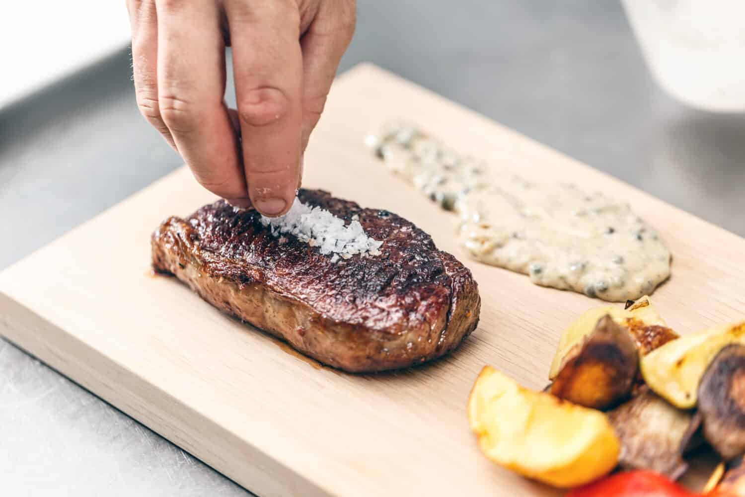 Chef decorate grilled T-bone steak with maldon salt