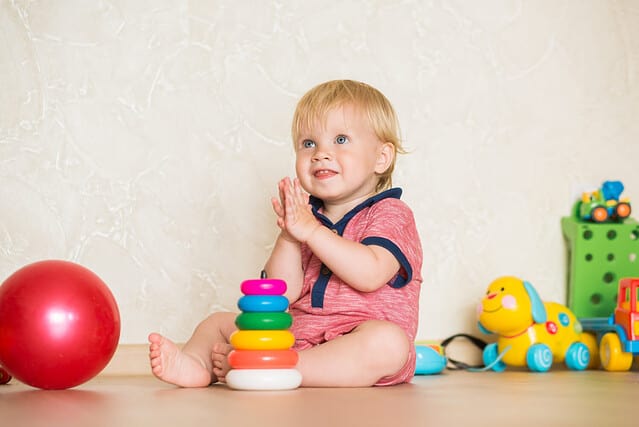 1,5 year-old child playing with educational cup toys at home. Little blond baby boy with blue eyes is playing with pyramid toy on the floor. Little kid have fun indoors