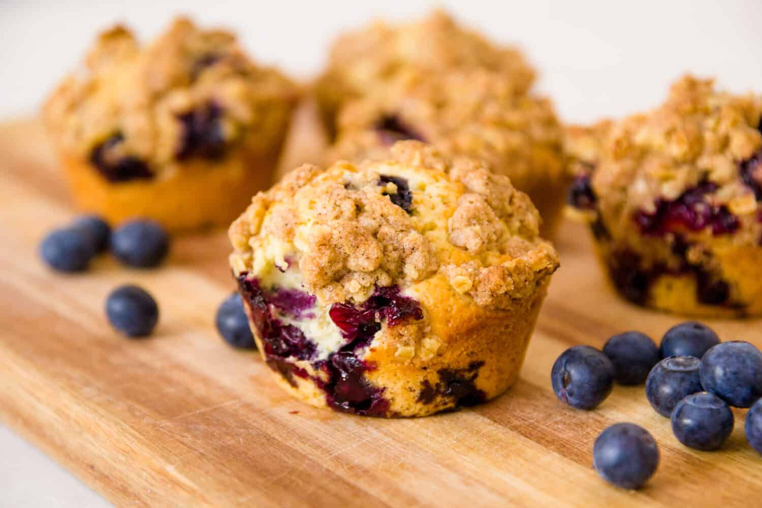 freshly baked blueberry muffins with an oat crumble topping on a natural wooden board