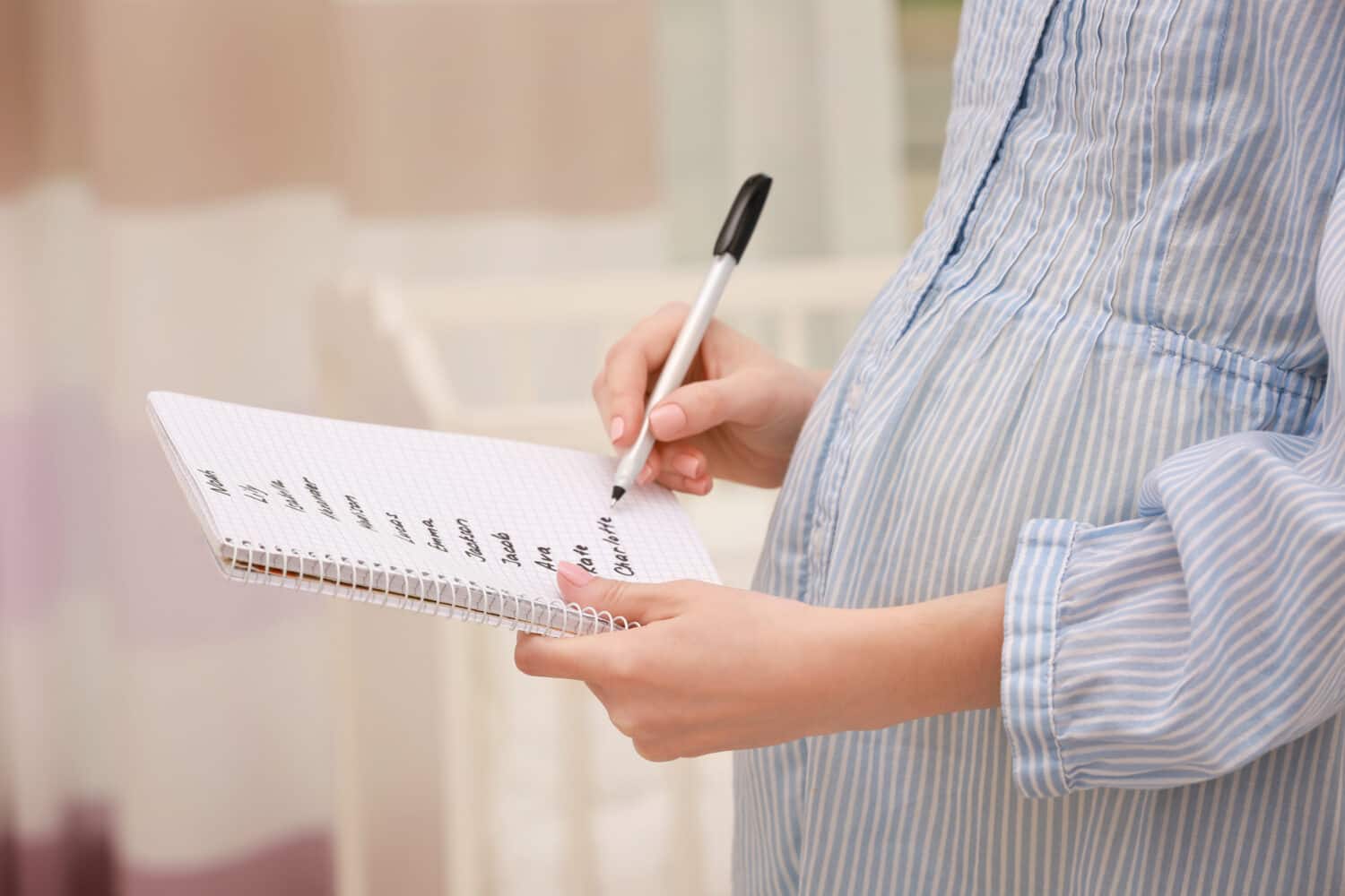 Pregnant woman writing baby names in notebook at home
