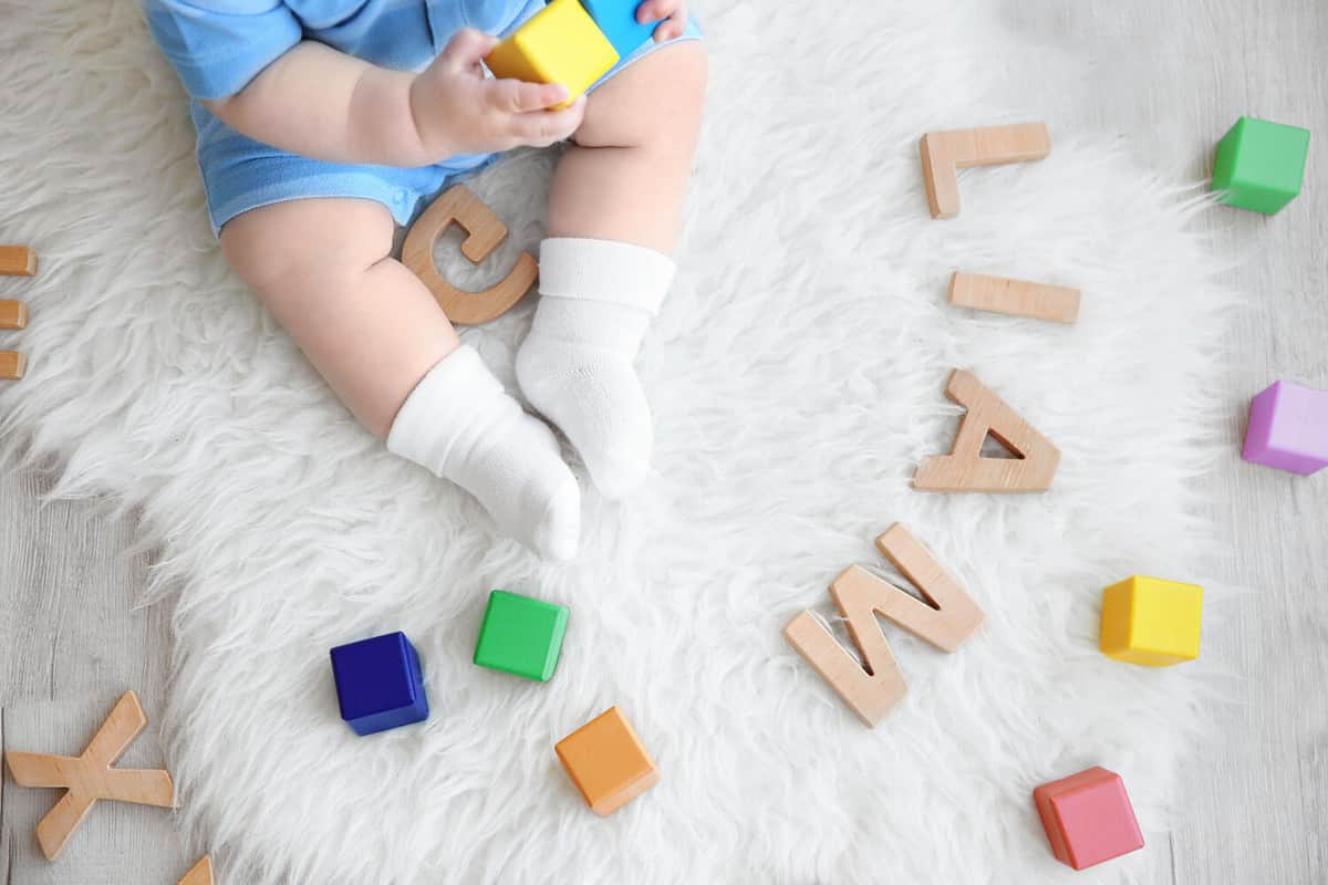 Cute baby sitting on floor with word LIAM composed of wooden letters. Choosing name concept