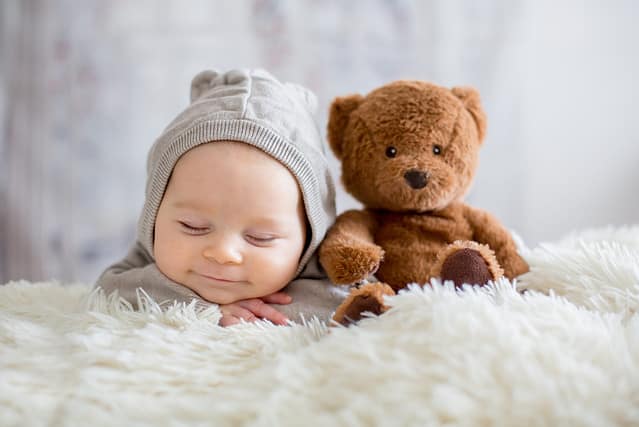 Sweet baby boy in bear overall, sleeping in bed with teddy bear stuffed toys, winter landscape behind him