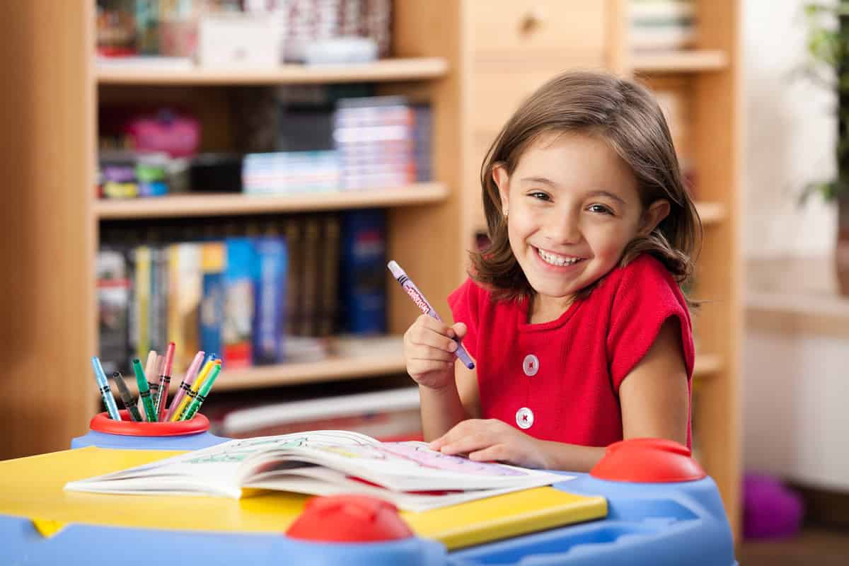 Little girl drawing on her book and having fun at playtable. Child learning to color at home or kindergarden.