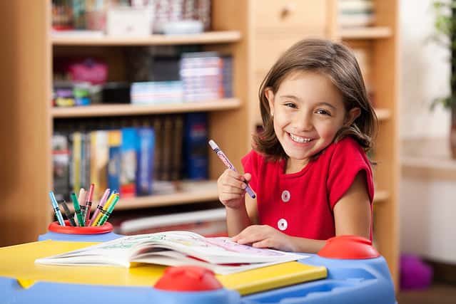 Little girl drawing on her book and having fun at playtable. Child learning to color at home or kindergarden.
