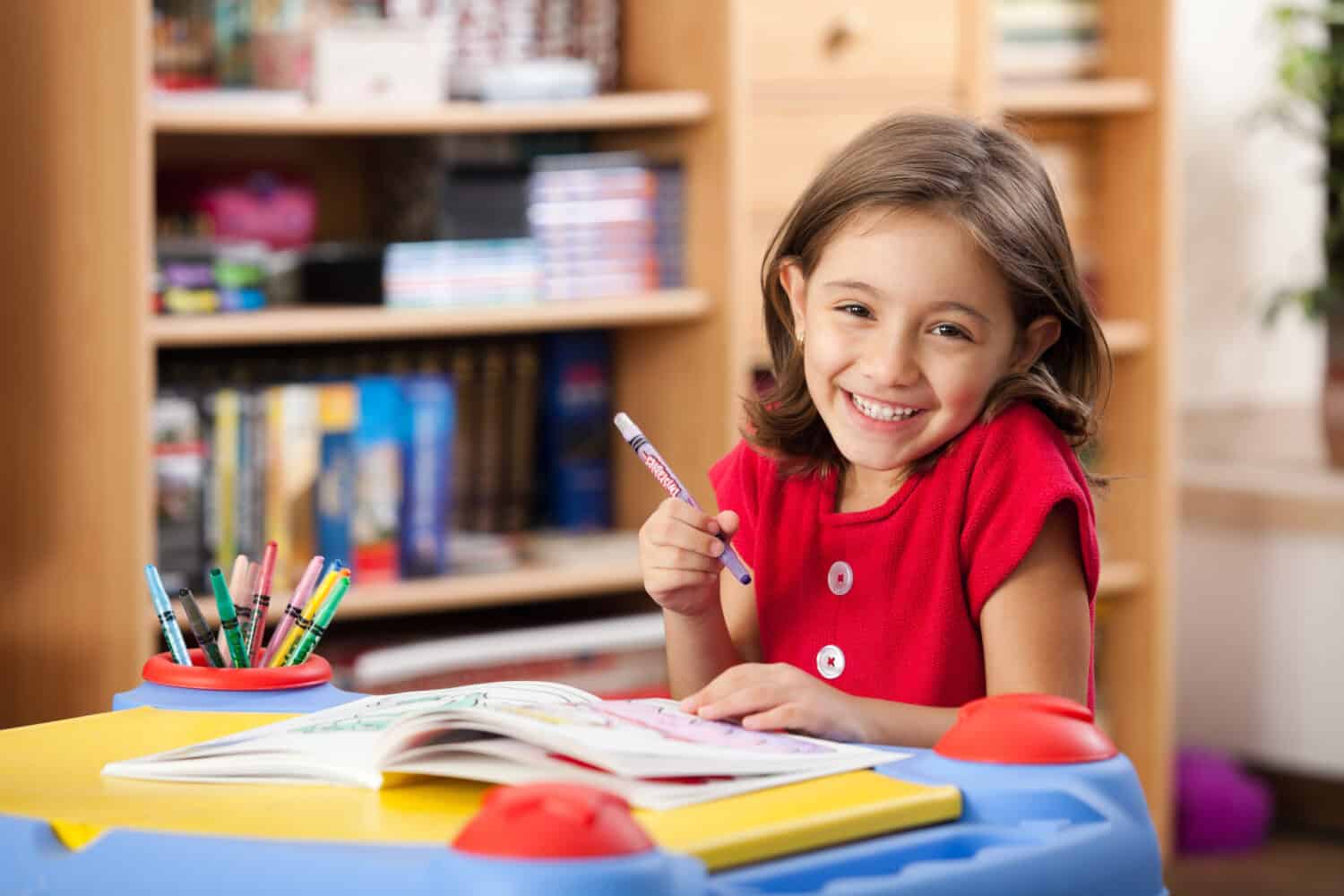 Little girl drawing on her book and having fun at playtable. Child learning to color at home or kindergarden.