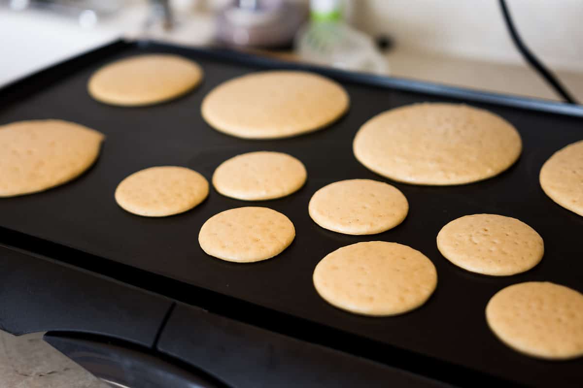 Various sized pancakes on black griddle