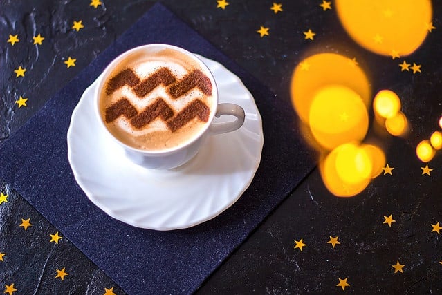 white cup of coffee with the symbol of the zodiac Aquarius on milk foam