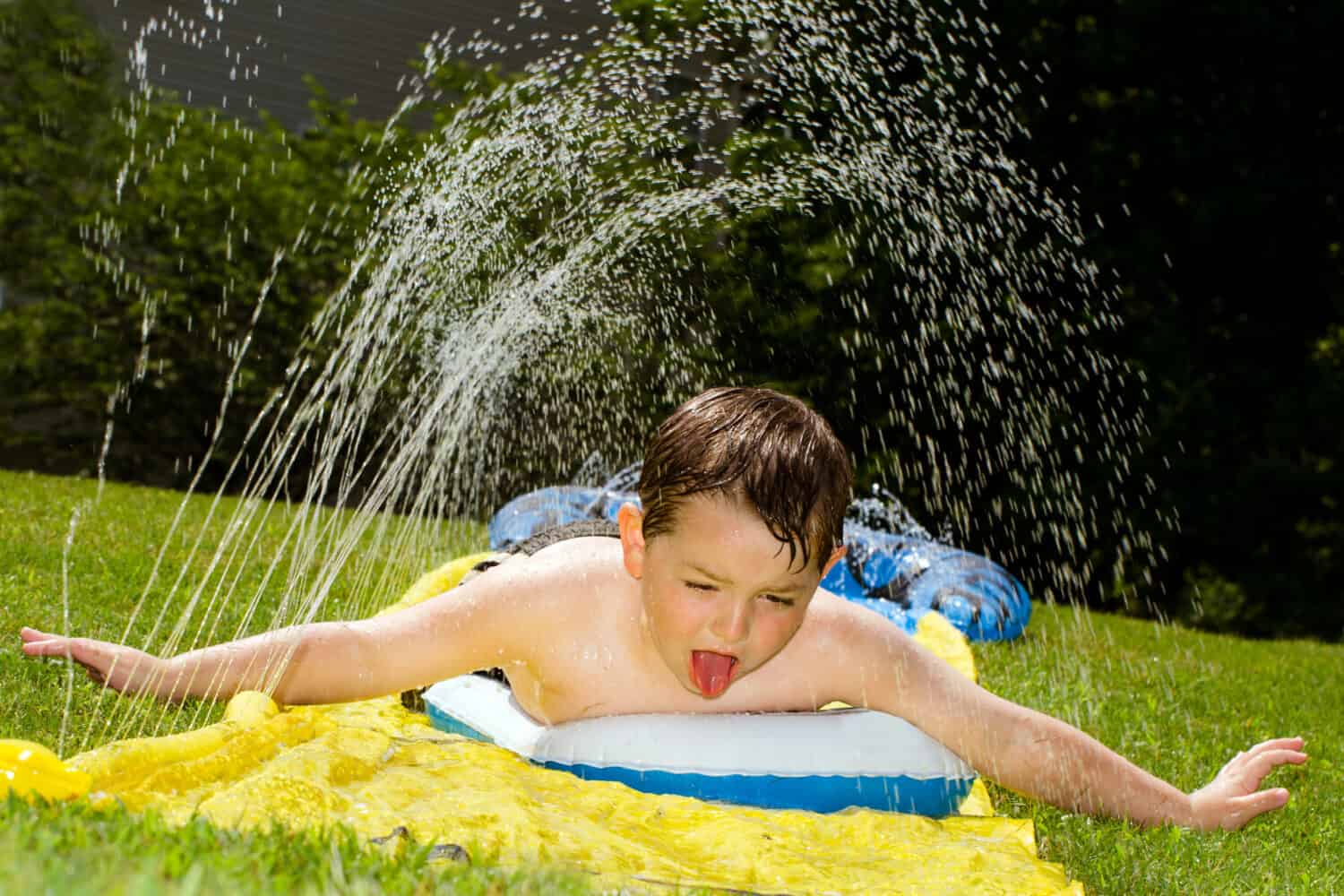 Happy child on water slide to cool off on hot day during spring or summer