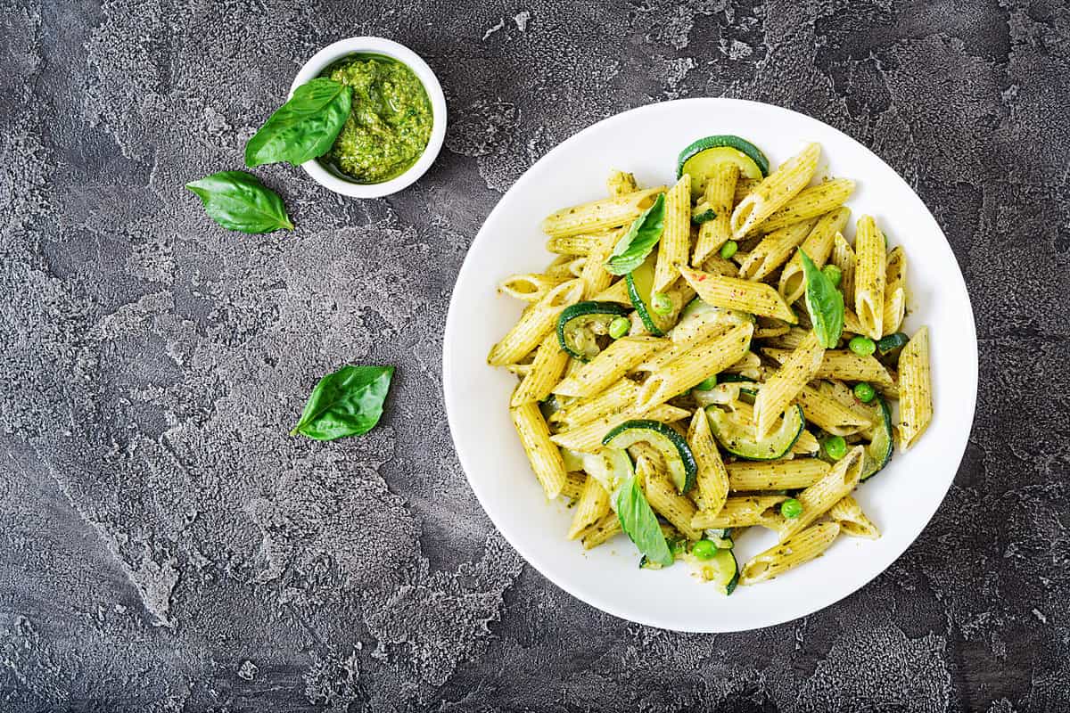 Penne pasta with pesto sauce, zucchini, green peas and basil. Italian food. Top view. Flat lay.