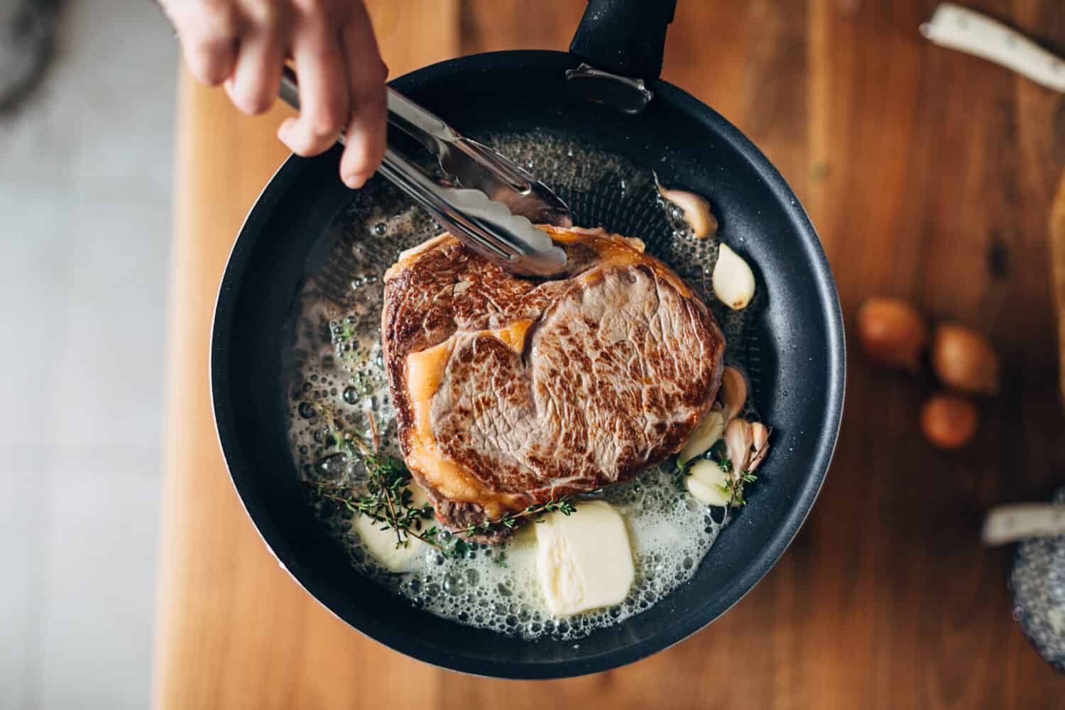 Overhead shot of chef preparing ribeye with butter, thyme and garlic. Keto diet.